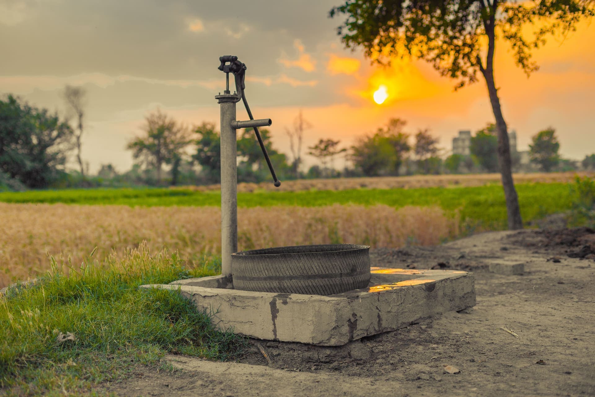An old water pump standing in farmland at sunset