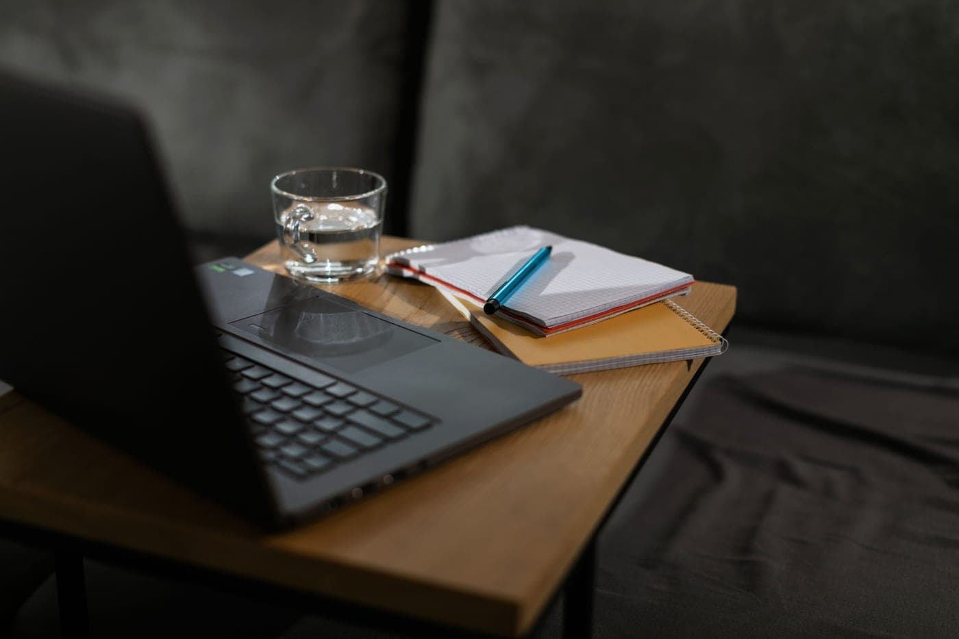 A notebook, pen and glass of water on a wooden desk