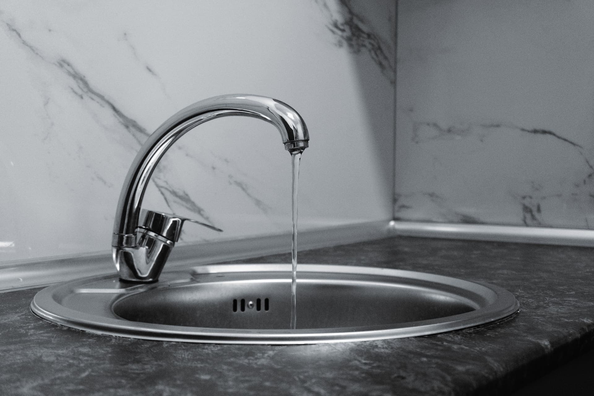 Chrome kitchen faucet running water over a sink