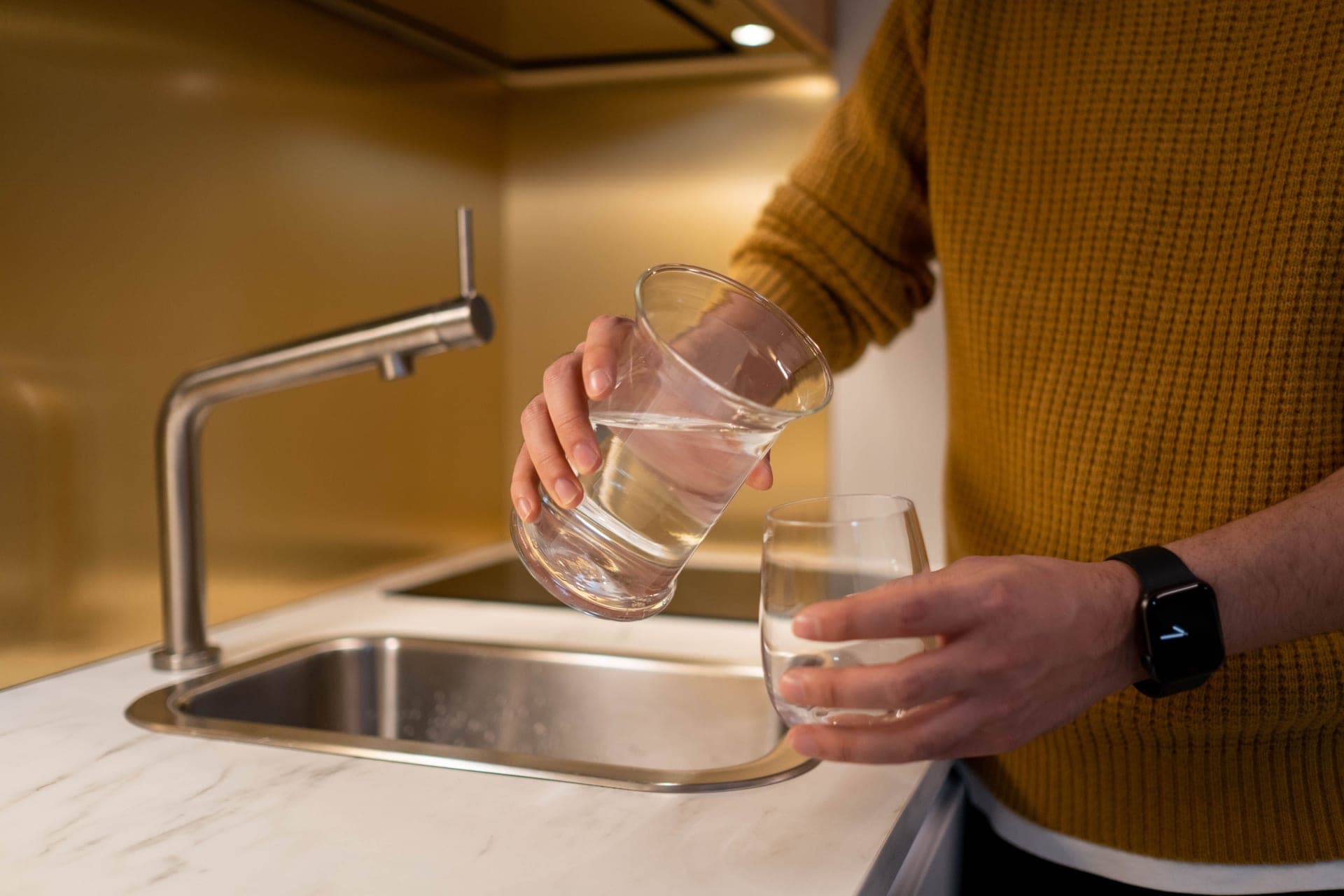 A person filling a glass at a kitchen tap
